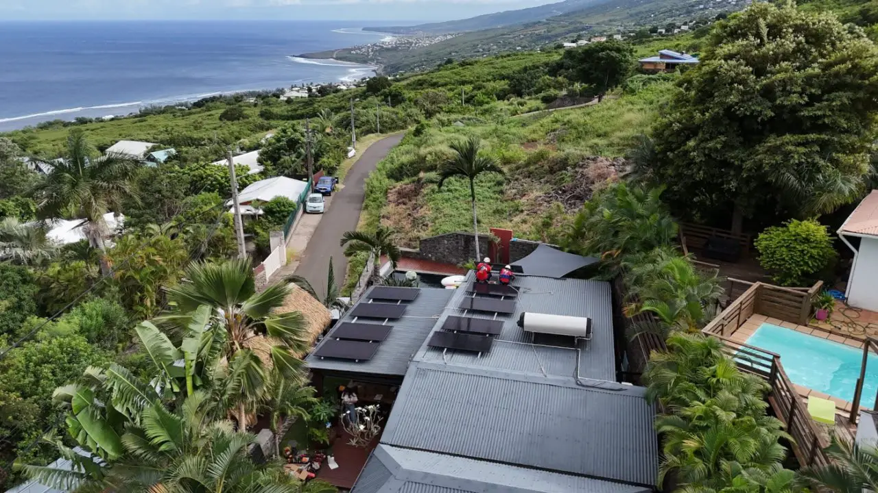 Techniciens de Solar Service en cours d'installation de panneaux photovoltaïques sur une villa avec piscine à La Réunion, vue sur la côte de l'île