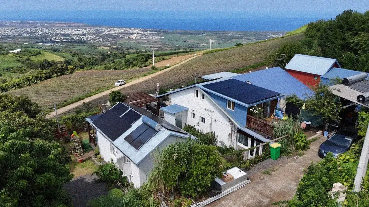 Vue aérienne de panneaux solaires photovoltaïques full black installés sur une toiture à La Réunion avec la côte ouest et l'océan Indien en arrière-plan